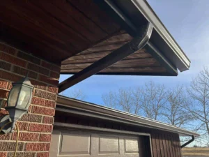 Close-up of newly installed seamless black gutters and wooden soffit on a brick house.